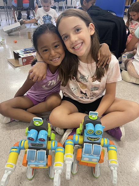 Two girls smiling while posing for a photo with their robot creations